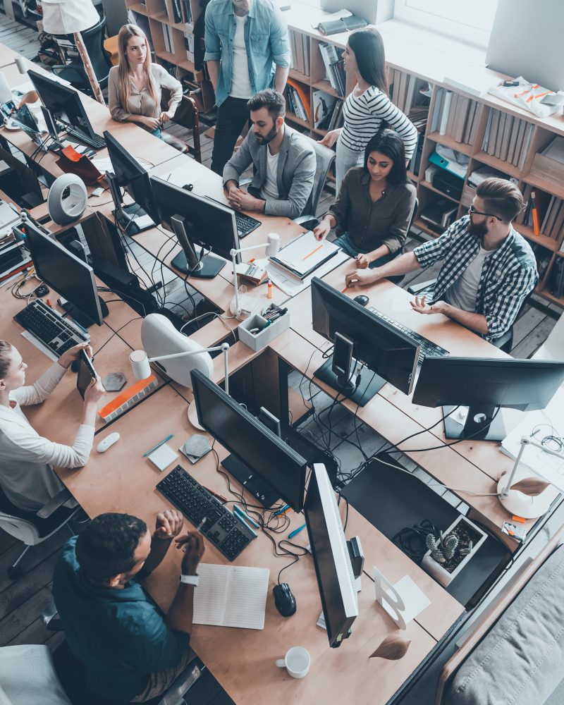 Successful young team at work. Top view of group of young business people in smart casual wear working together while sitting at the large office desk