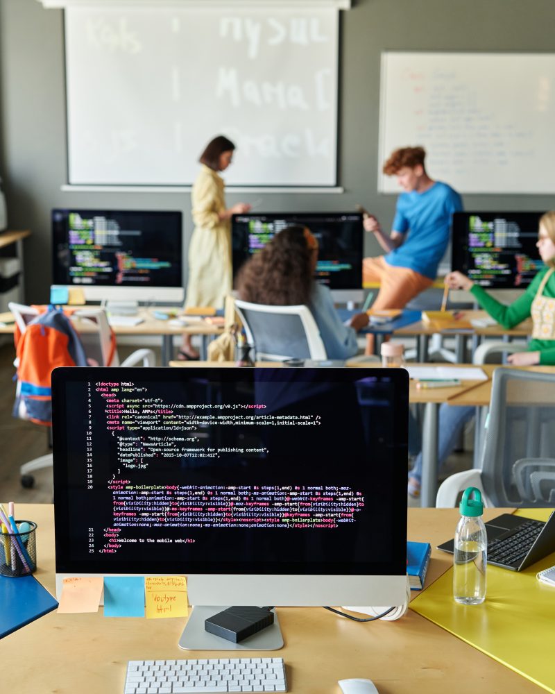 Vertical background image of classroom with computer on desk in IT class in school and code lines on screen